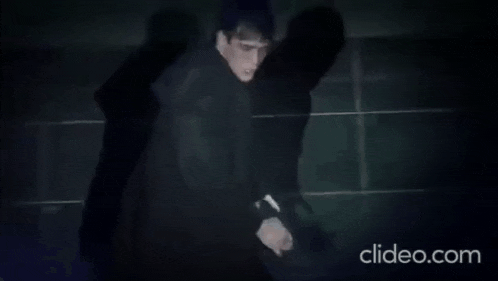 a man in a black shirt is standing in a dark room with a shadow on the floor .