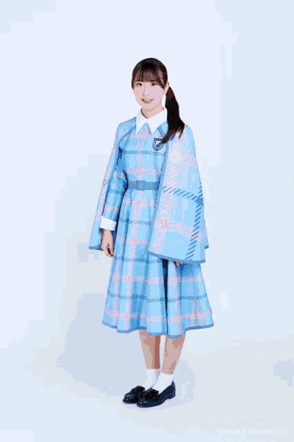 a girl wearing a blue and pink plaid dress is standing in front of a white wall