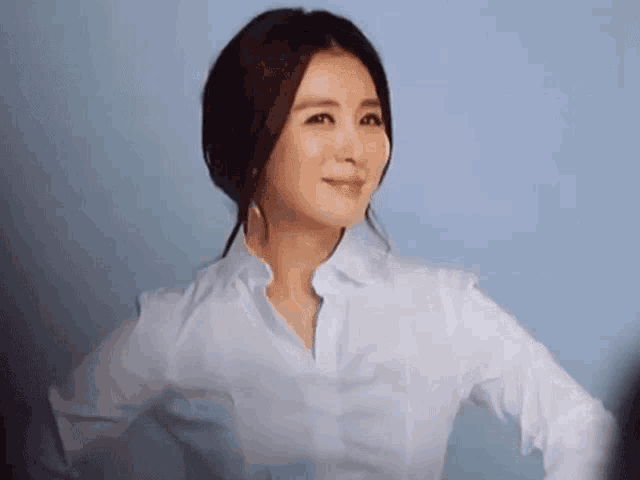 a woman wearing a white shirt is standing with her hands on her hips .