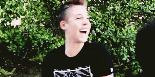 a young man in a black shirt is laughing in front of a tree .