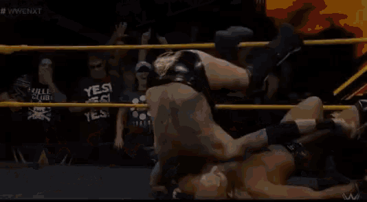 a referee is standing in the middle of a wrestling ring watching a wrestler .