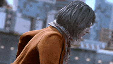 a woman wearing a scarf and an orange coat is looking down