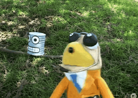 a stuffed animal is standing in the grass next to a can that has a face on it