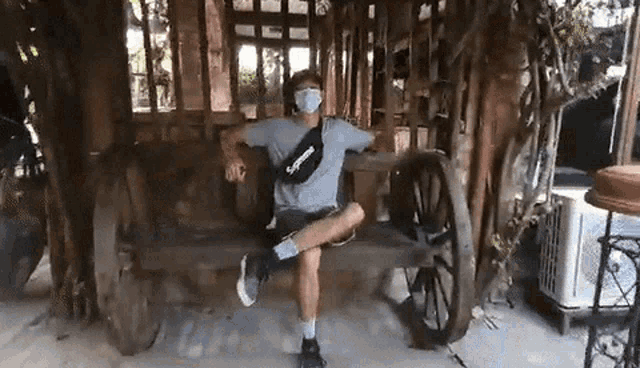 a man wearing a mask is sitting on a wooden bench with his leg up