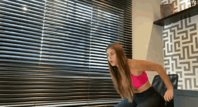 a woman in a pink sports bra is doing exercises on a chair in front of a window .