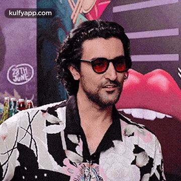 a man wearing sunglasses and a floral shirt is standing in front of a poster of a woman 's mouth .