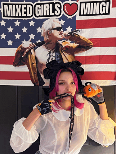 a girl with pink hair stands in front of a mixed girls mingi banner