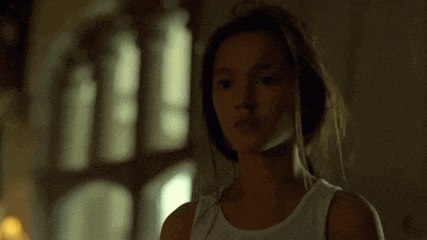 a young woman in a white tank top is standing in a dark room .