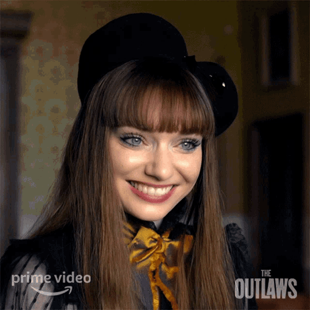 a woman wearing a black hat is smiling in front of a poster for the outlaws on prime video