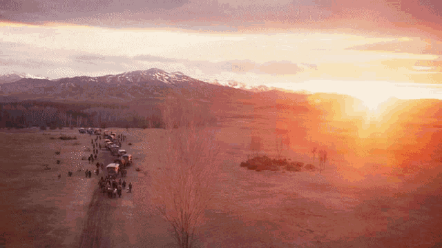 a group of people standing in a field with mountains in the background at sunset