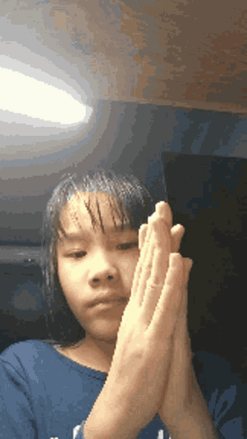 a girl in a blue shirt is praying with her hands folded