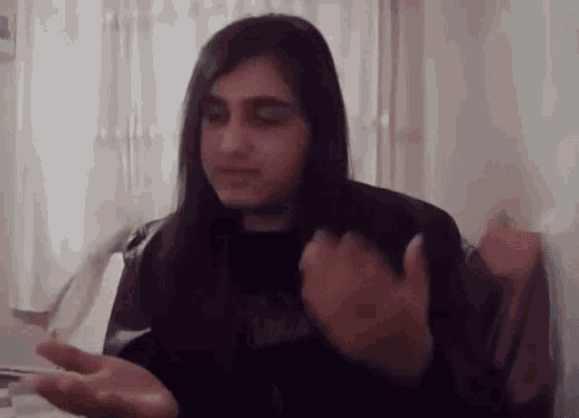 a woman with long hair is sitting at a table with her hands out .