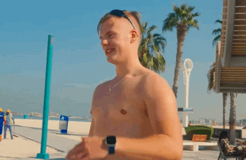 a man without a shirt is standing on a beach with palm trees and a sign that says ' a ' on it