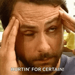 a man with a beard is holding his head in pain and says `` hurtin ' for certain '' .