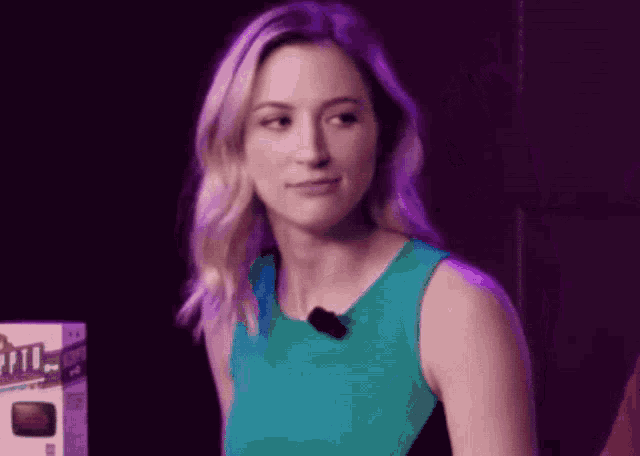 a woman in a green tank top with a microphone on her neck is looking at the camera .