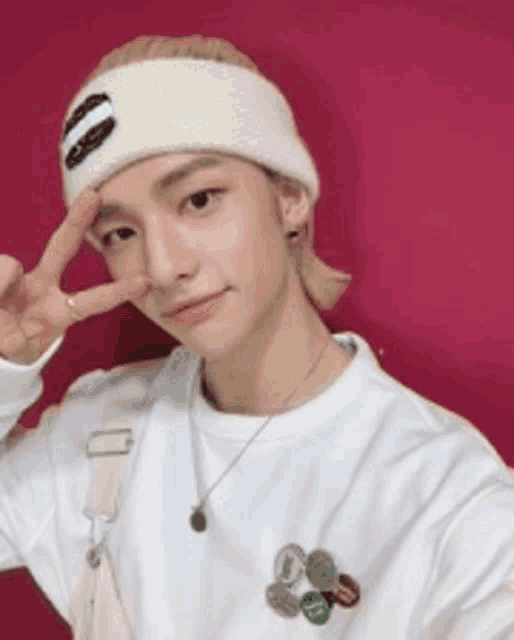 a young man wearing a white headband and a white sweater is giving a peace sign .
