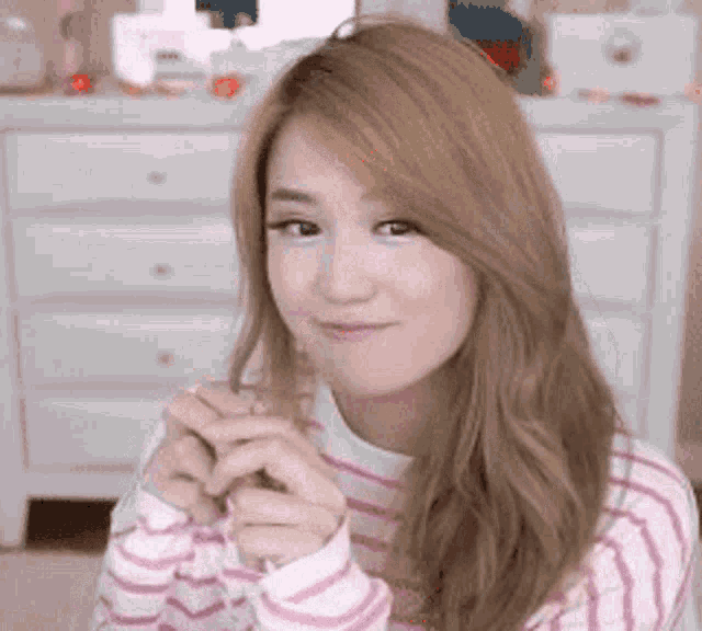 a woman in a pink and white striped sweater is making a heart with her hands .