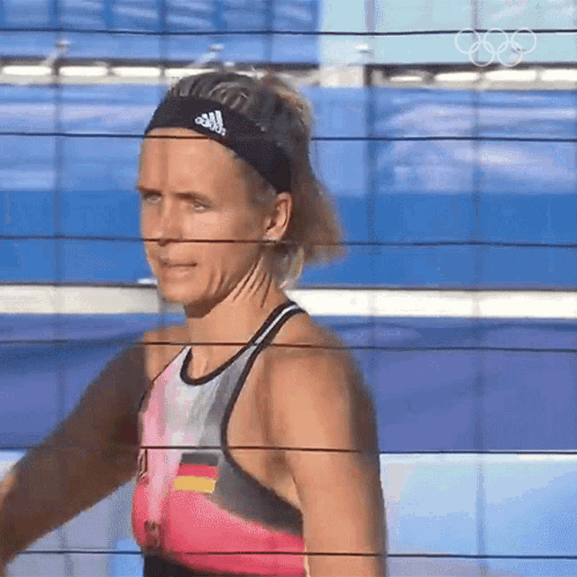 a woman wearing an adidas headband stands behind a volleyball net