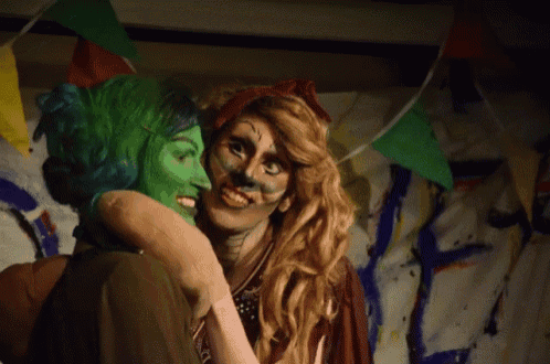 a woman with green face paint is hugging another woman with red hair