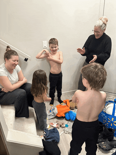 a group of people are gathered in a room including a shirtless boy and two girls