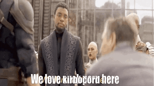 a man in a suit is standing in front of a group of people and says we love kirbocord here .
