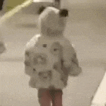 a little girl is standing on a sidewalk wearing a white coat and a hat .