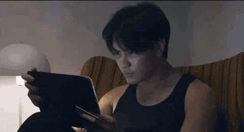 a man in a black tank top is sitting on a couch using a tablet computer .