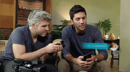 two men are sitting on a couch looking at a cellphone