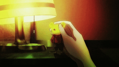 a hand is holding a small yellow object in front of a lamp