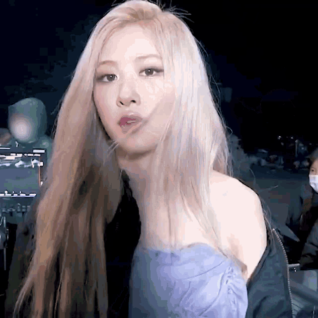 a close up of a woman with long blonde hair wearing a blue dress and a bomber jacket .