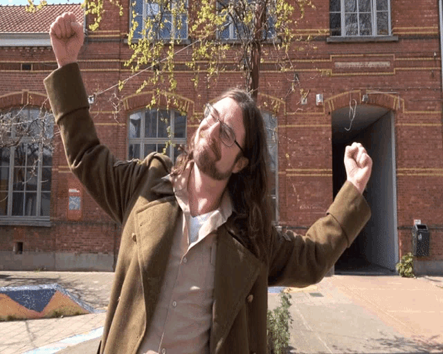 a man with his arms in the air stands in front of a brick building