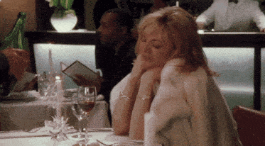a woman in a fur coat sits at a restaurant table with wine glasses