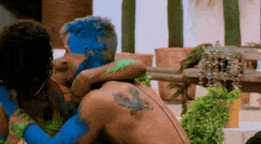 a man with a bird tattoo on his back is hugging a woman with blue paint on her face
