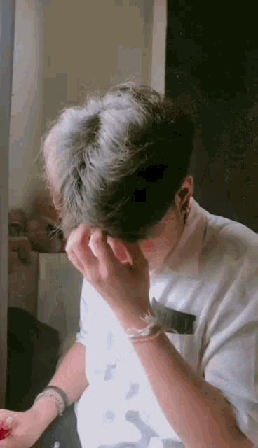 a young man is sitting in front of a mirror covering his face with his hand .