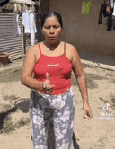 a woman in a red tank top and floral pants is giving a thumbs up in a yard .