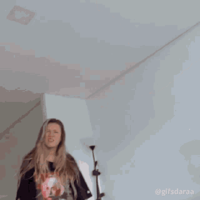 a woman with long blonde hair is making a funny face while standing in front of a wall .