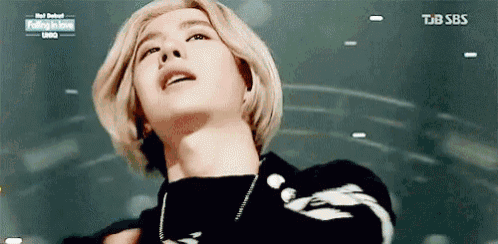 a man with blonde hair is wearing a black sweater and a necklace .