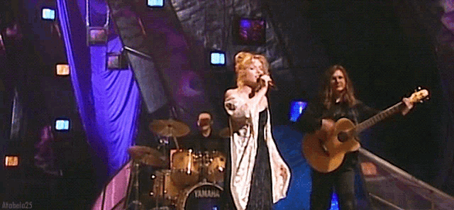 a woman singing into a microphone while a man plays a guitar on a stage
