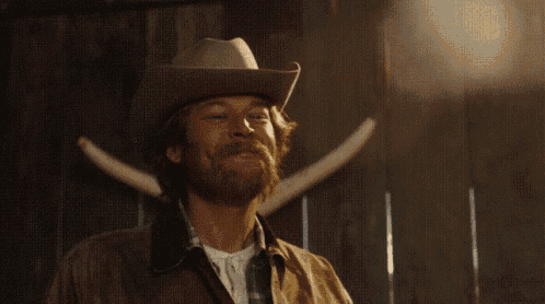 a man wearing a cowboy hat stands in front of a wall with horns on it