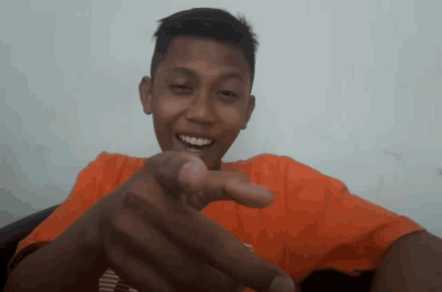 a boy in an orange shirt is pointing his finger at the camera