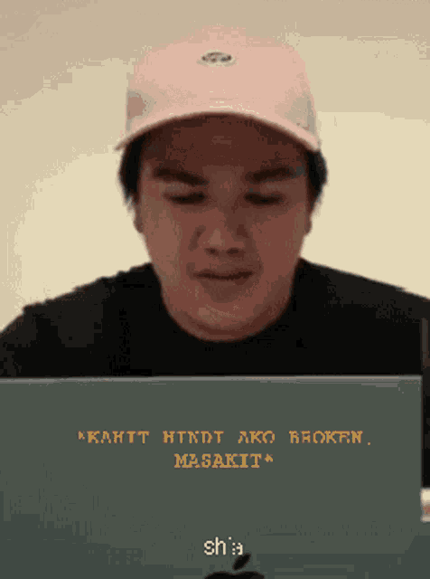 a man wearing a pink hat is looking at a laptop screen that says " kahit hindi ako broken "