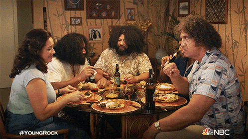 a group of people are sitting around a table eating food and drinking from bottles sponsored by nbc