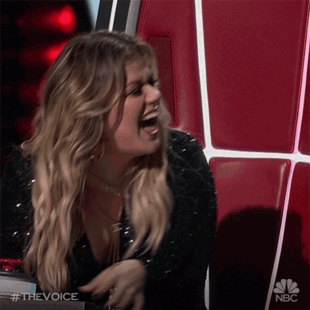 a woman is laughing while sitting in a chair with a nbc logo in the background