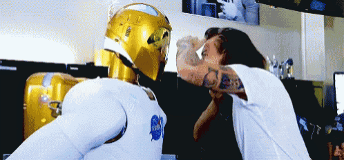 a man with a tattoo on his arm is standing next to a gold nasa robot