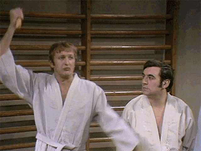 two men in white kimonos are standing next to each other in a gym