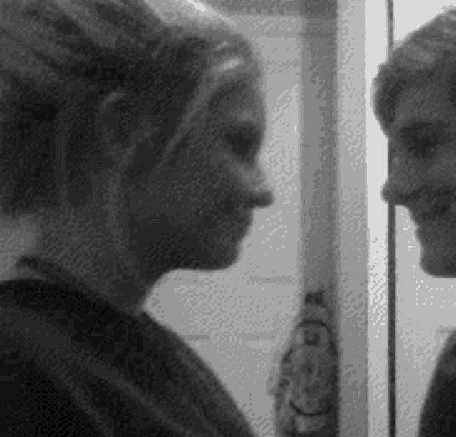 a woman is looking at her reflection in a mirror and smiling .