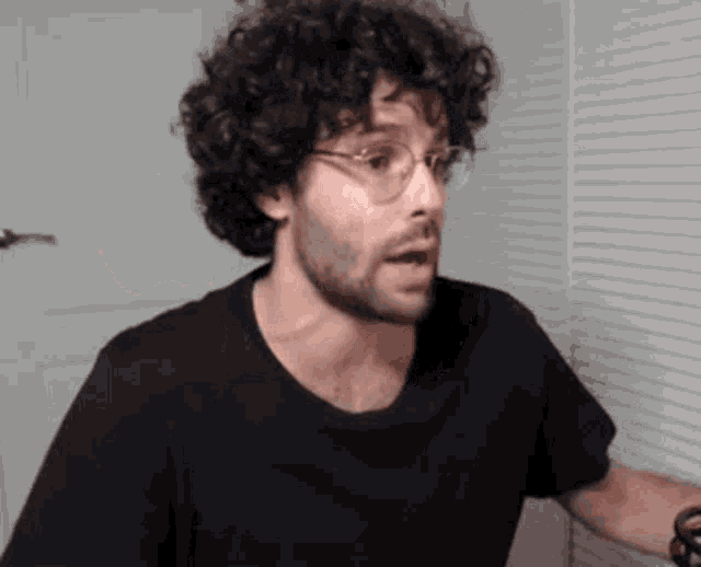 a man with curly hair is wearing glasses and a black shirt .