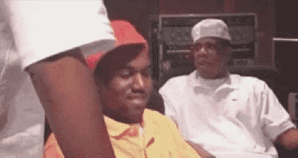 a man wearing a red hat and a yellow shirt is sitting next to another man in a white shirt .