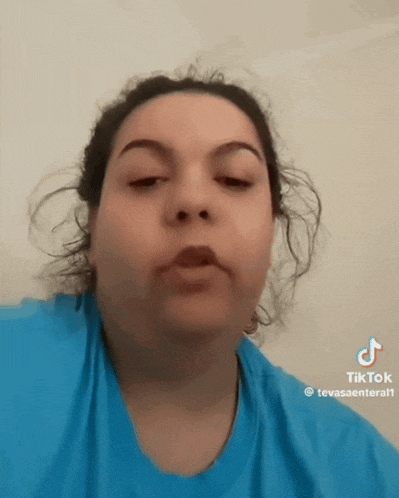a woman wearing a blue shirt is making a funny face with tik tok written on the bottom right