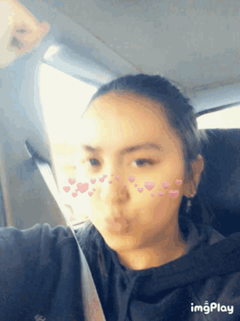a girl is taking a selfie in a car with hearts on her face and the words imgplay at the bottom